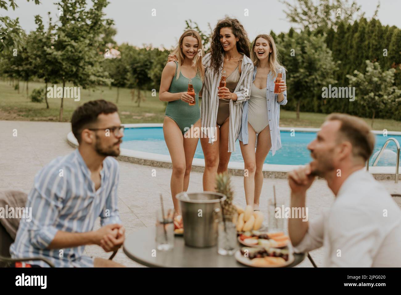 Group of happy young people cheering with drinks and eating fruits by the pool in the garden Stock Photo
