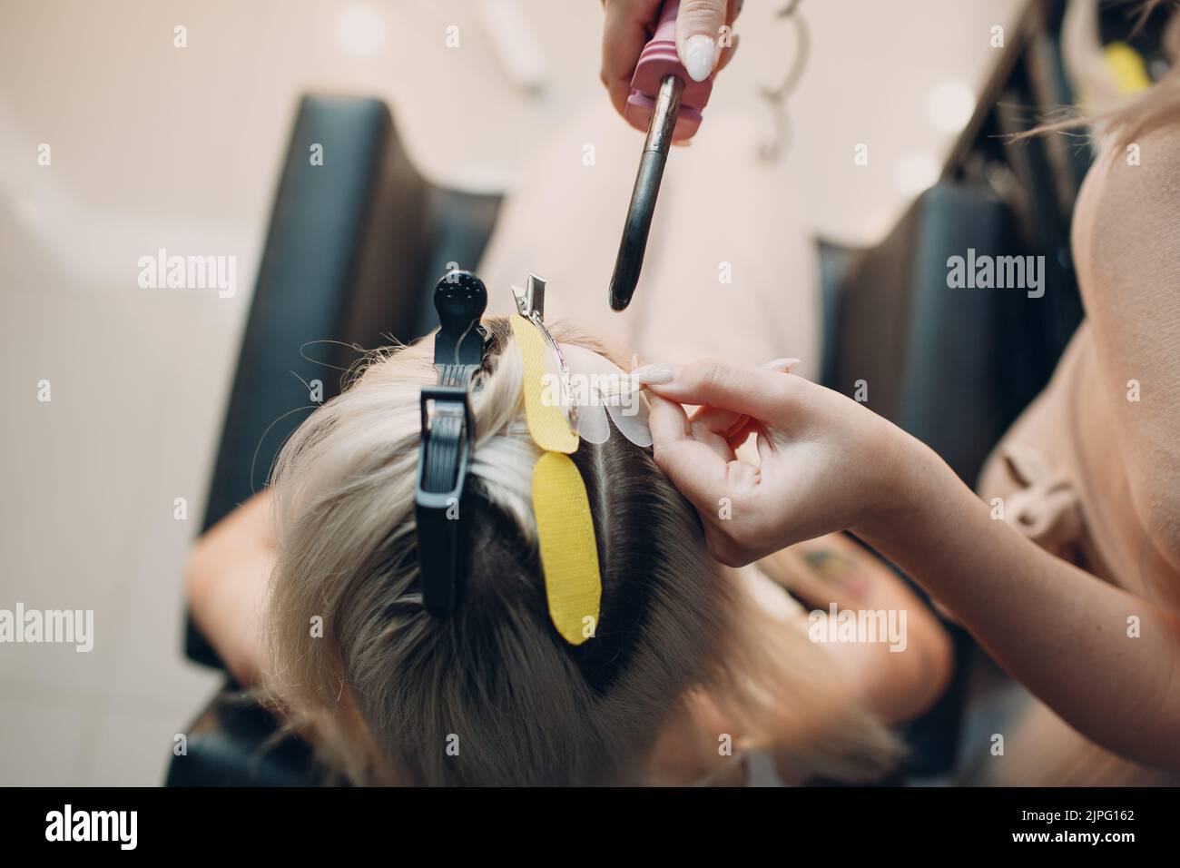 Hairdresser female making hair extensions to young woman with blonde
