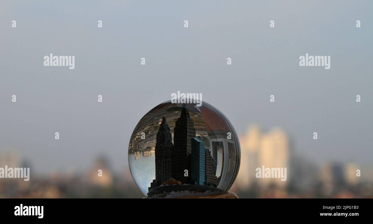 Toy buildings inside a souvenir crystal globe against a real town with soft focus Stock Photo