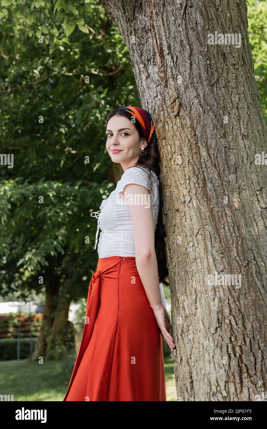 Pretty model in blouse and skirt standing near tree in park Stock Photo