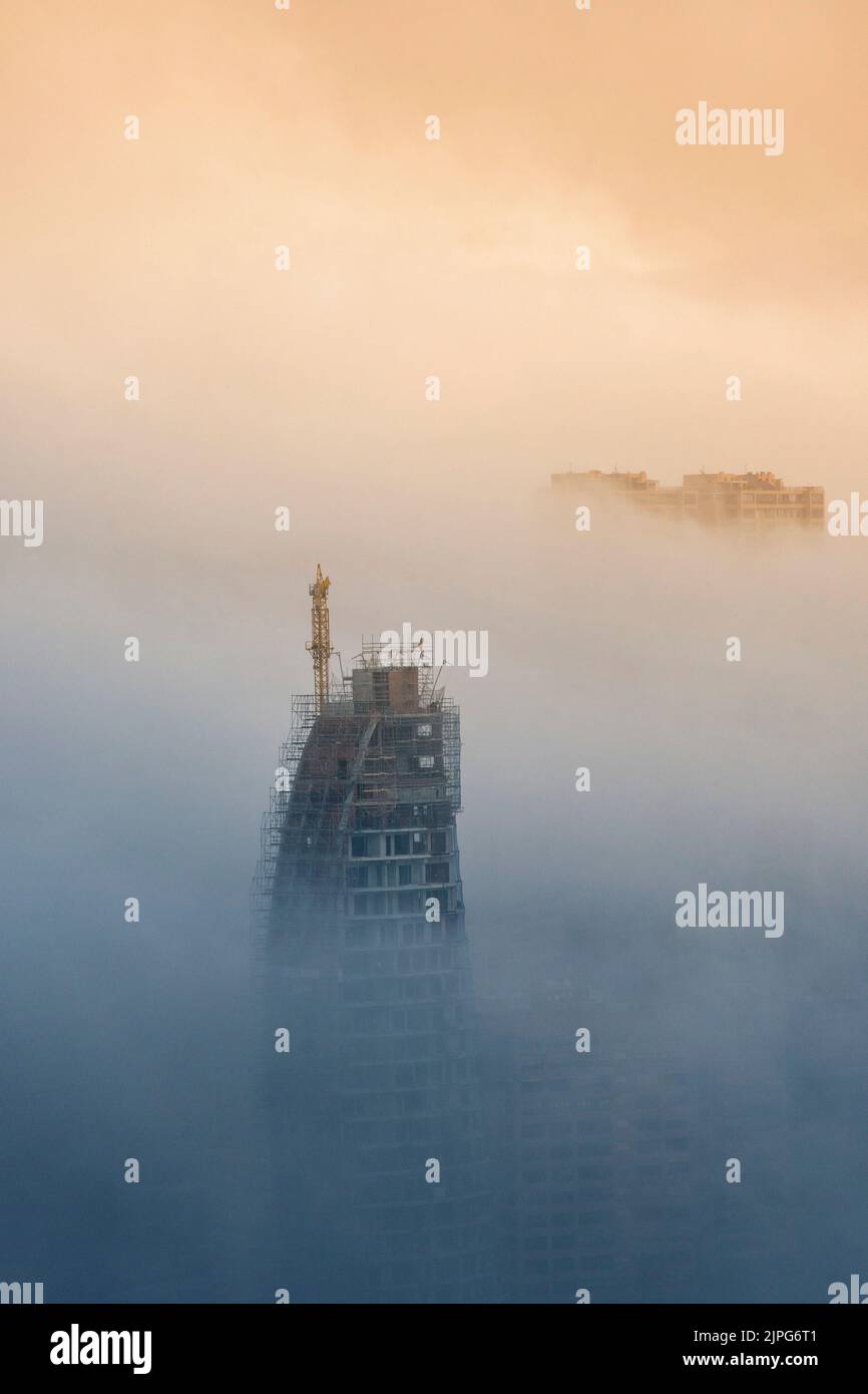 The top of a skyscraper under construction rises out of the fog in Benidorm, Spain Stock Photo