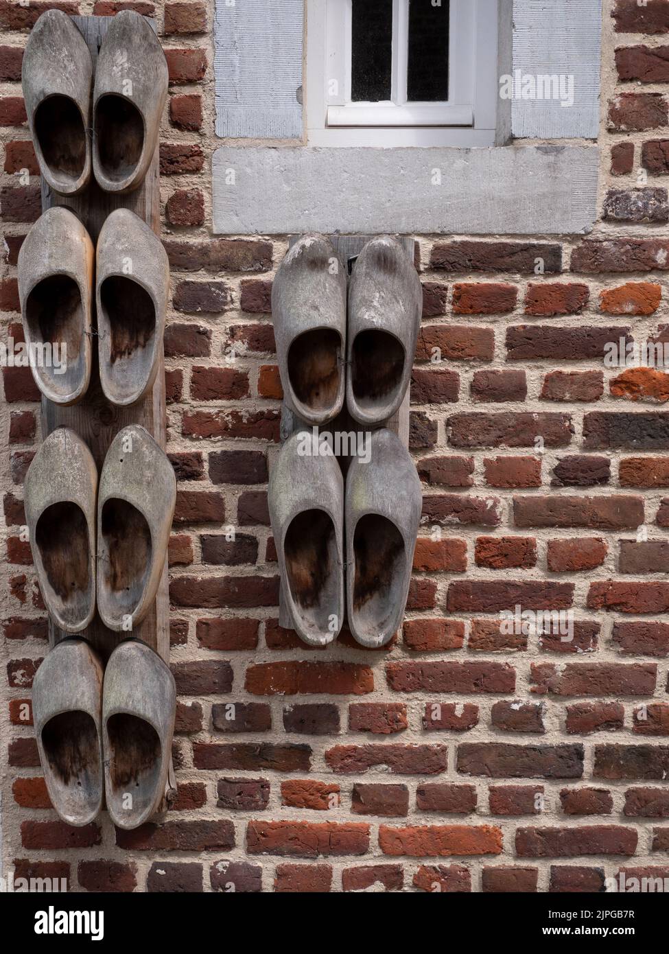 Wooden clogs attached to an old brick wall with a small window Stock Photo