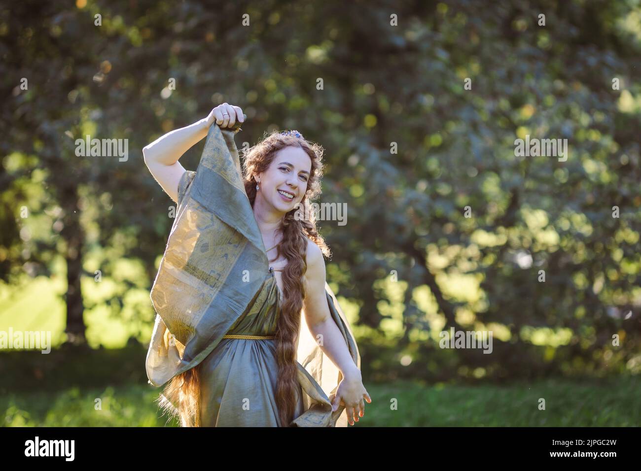 Portrait of a beautiful mature woman dressed in a nymph-style dress inspired by early 20th century artists.Happy woman in the garden on a sunny day Stock Photo