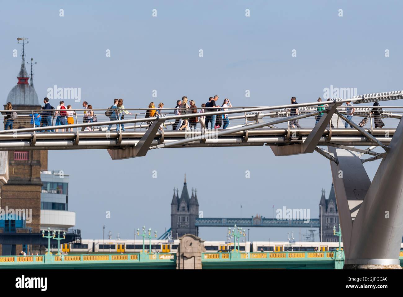 People walking across the Millennium Bridge over the River Thames, London, UK, in front of Tower Bridge. People, train and bridges crossing Thames Stock Photo