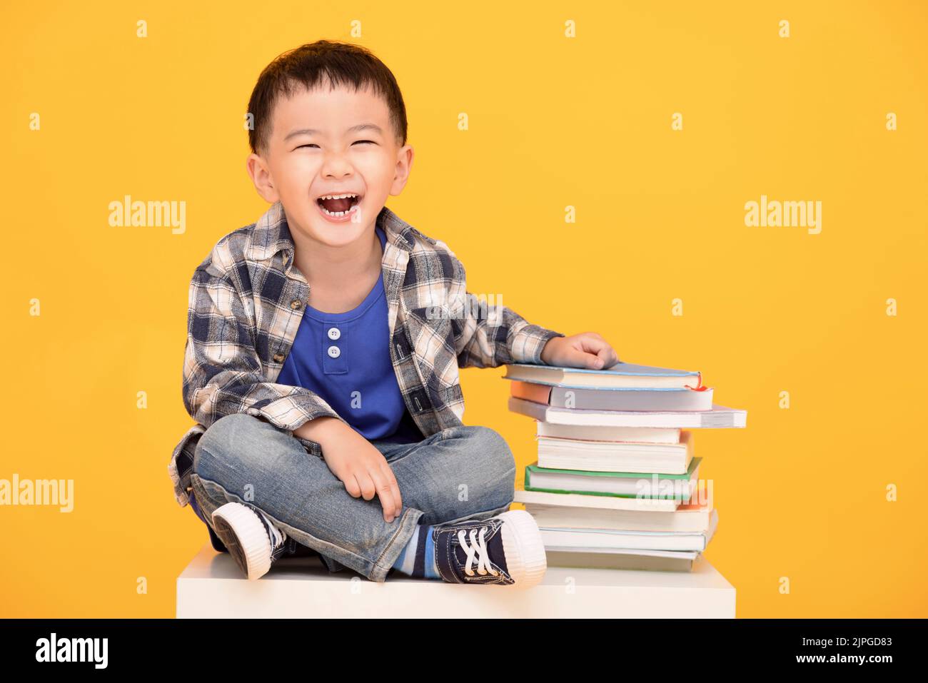 Happy kid sitting with books isolated on yellow background Stock Photo