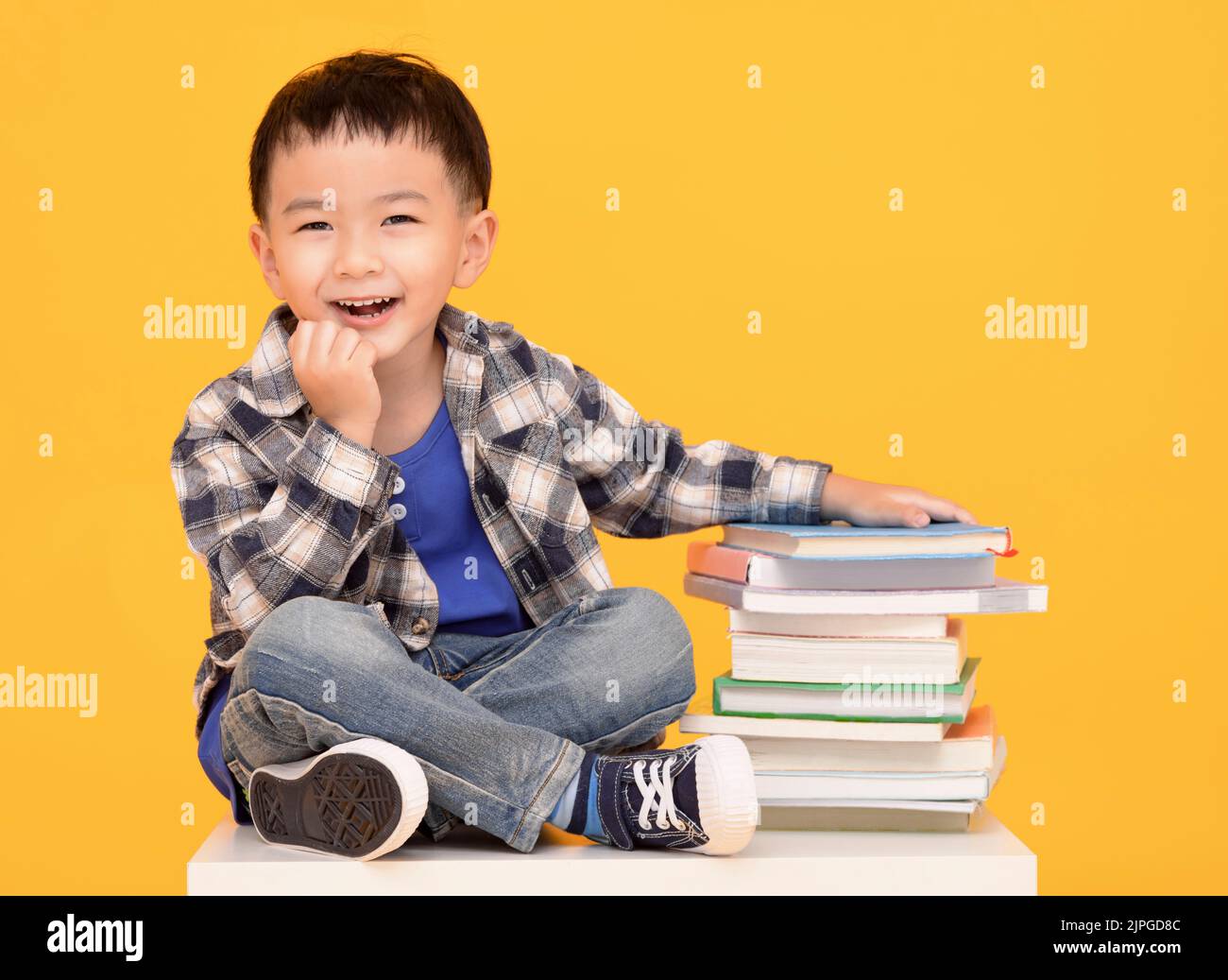 Happy little boy sitting with books isolated on yellow background Stock Photo