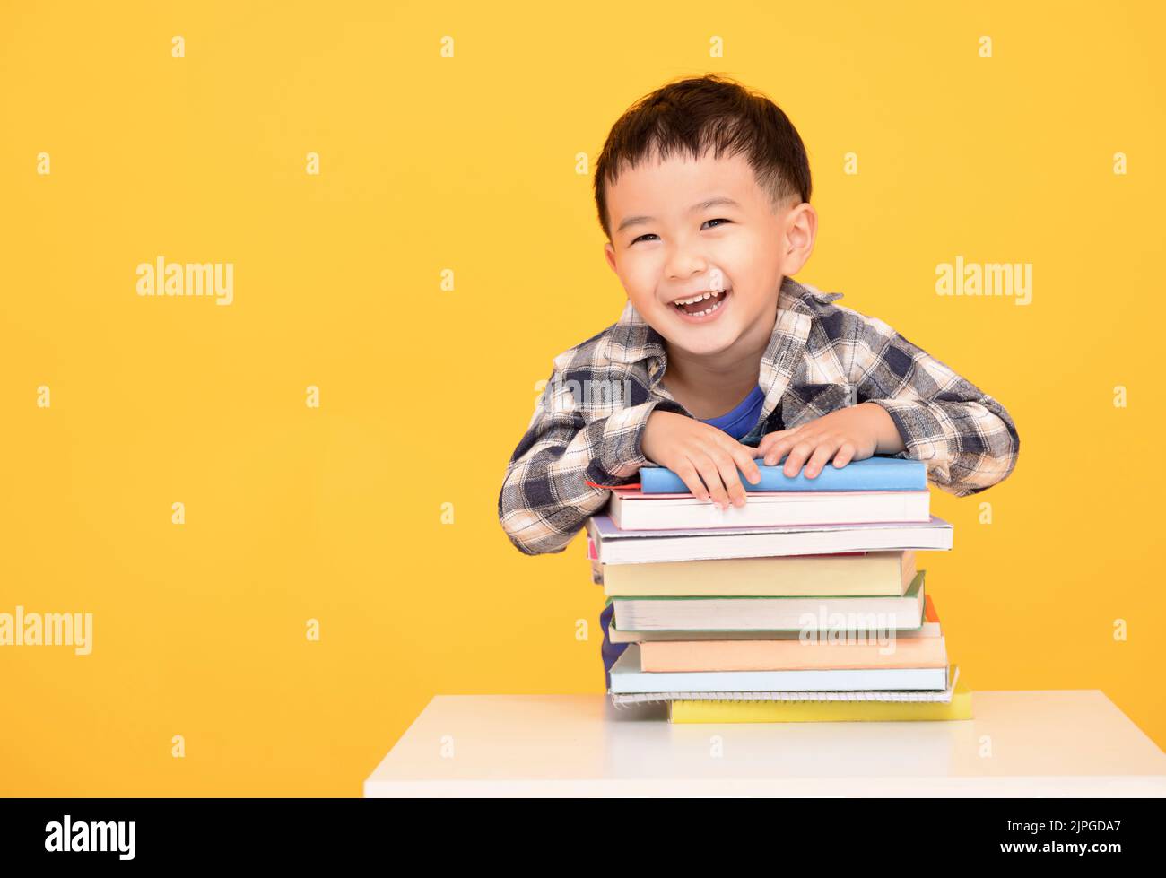 Happy little boy holding large books isolated on yellow background Stock Photo
