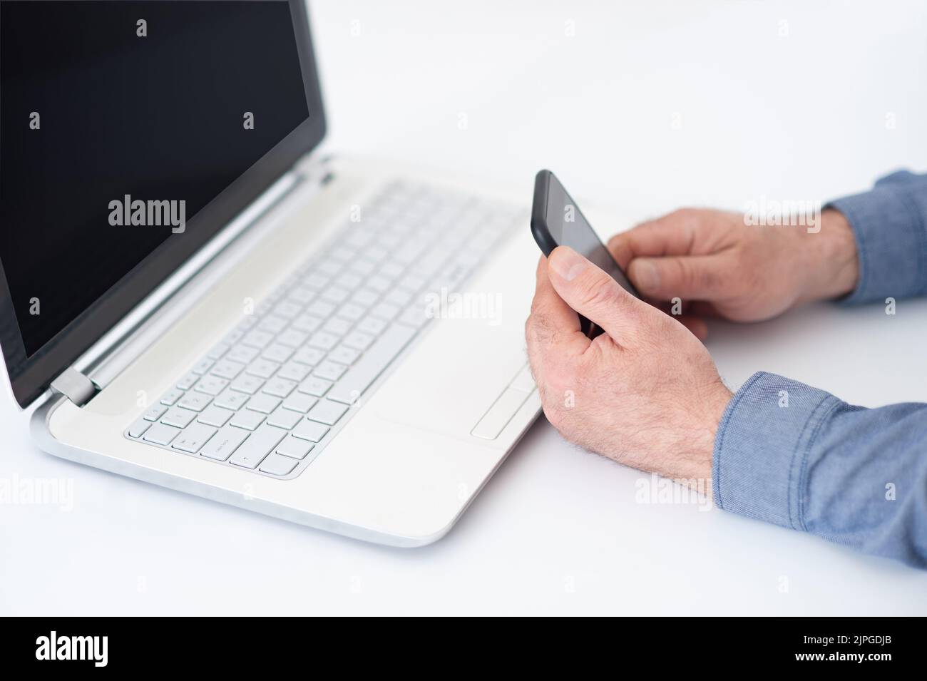 Man's hand using the phone and compute laptop. Online work on office table. Laptop with space for text. Trending cryptocurrency trading concept. Stock Photo