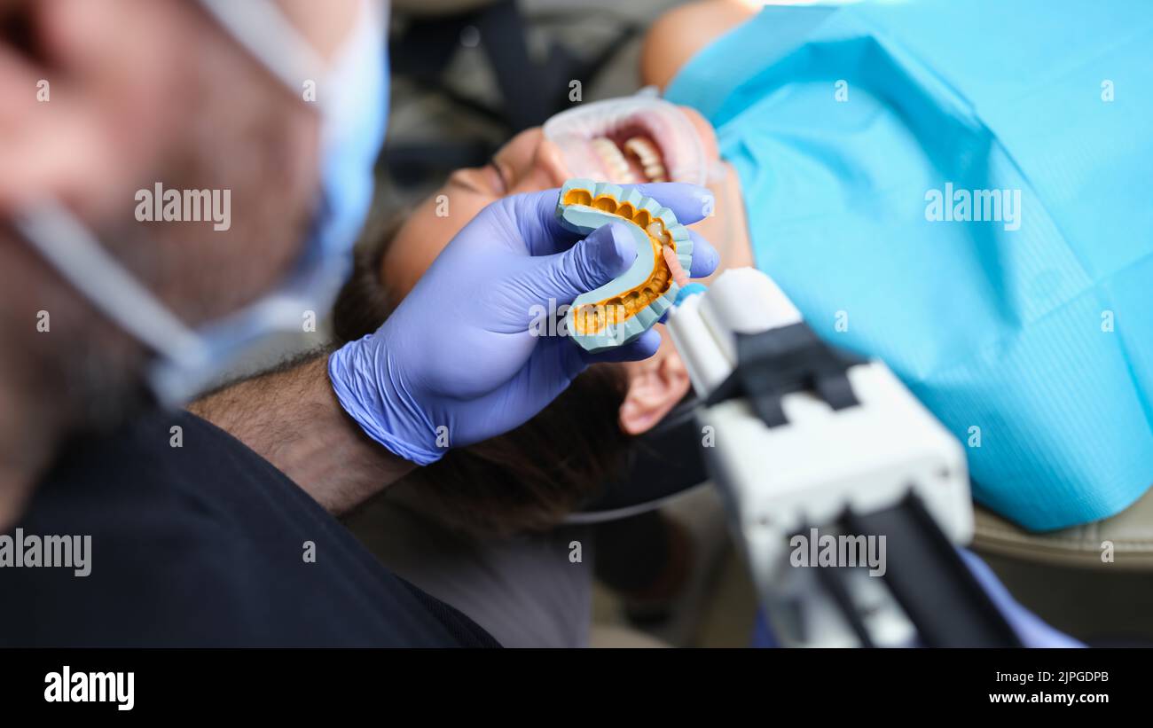 Dentist holds cast with veneers on plaster model and patient in dental