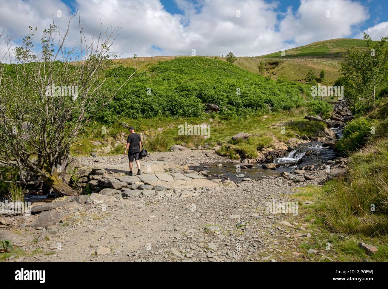 Man walking along path across Roughten Gill on Blease Fell towards Lonscale Fell in summer near Keswick Lake District National Park Cumbria England UK Stock Photo