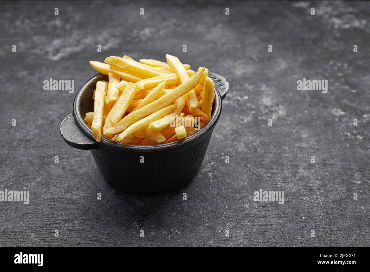 French fries in cast iron on gray concrete with space for text Stock