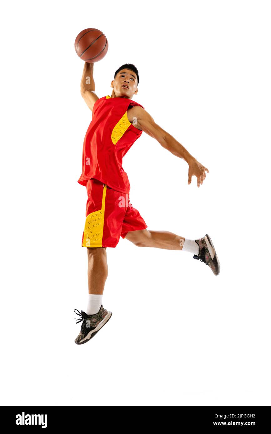 Portrait of young man, basketball player jumping, training, throwing ball into basket isolated