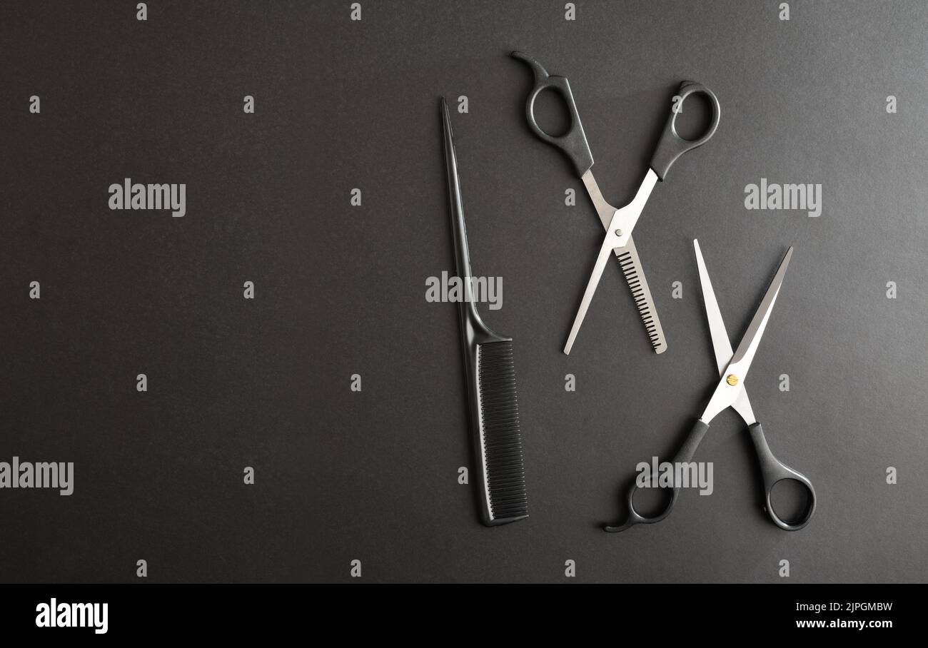 Basic conceptual hairdressing background with two scissors and comb on a black background and space to write. Top view. Horizontal composition. Stock Photo