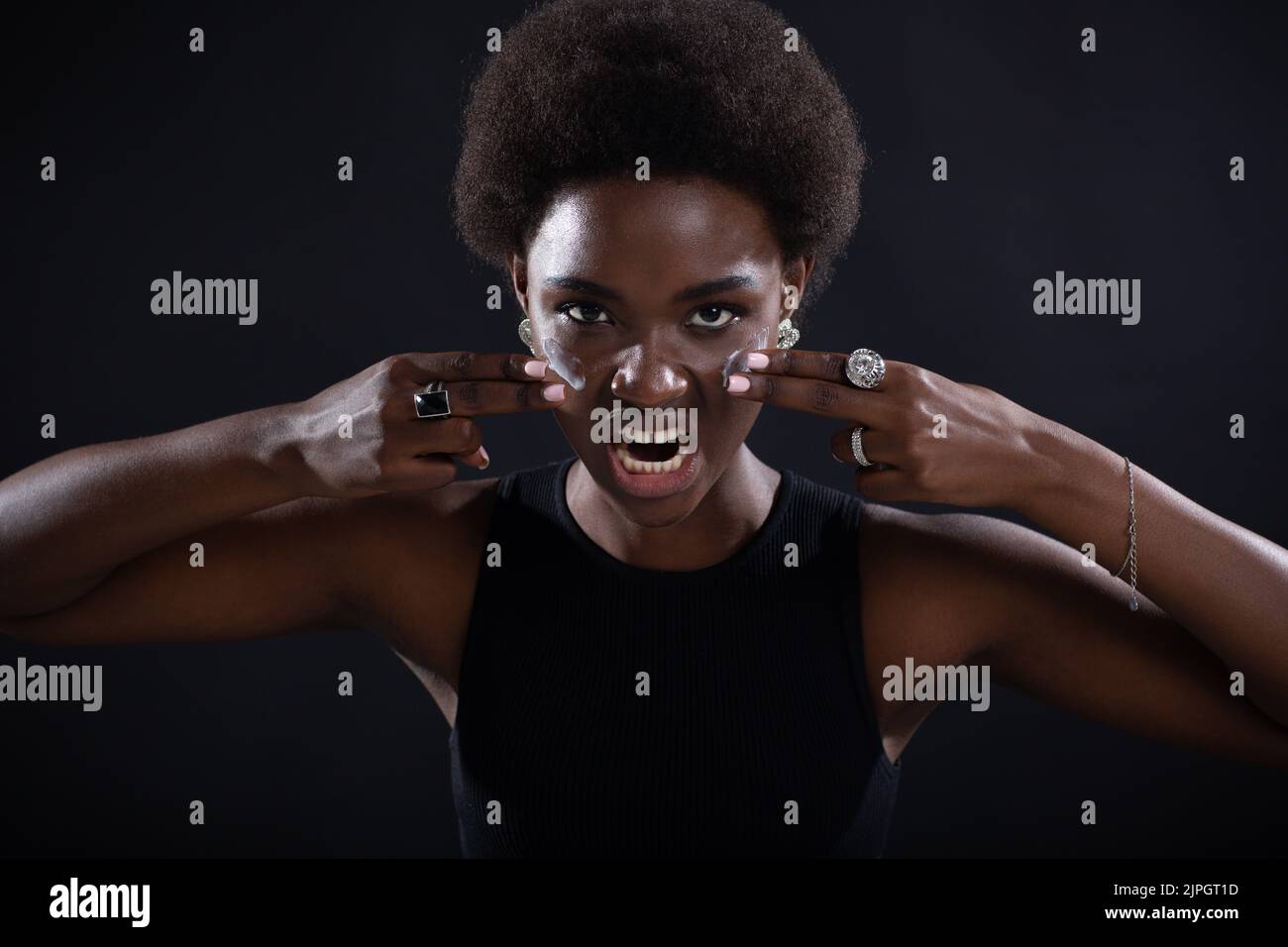 Beautiful young ethnic african american black woman applying by fingers white cream on her face with emotion like american football player Stock Photo