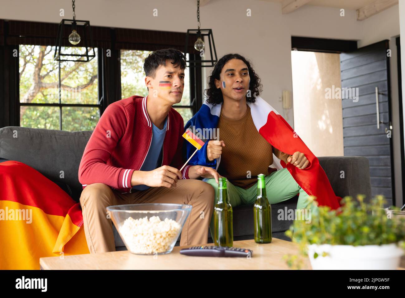 Happy biracial male couple sitting on sofa, supporting and holding flags of germany and france Stock Photo