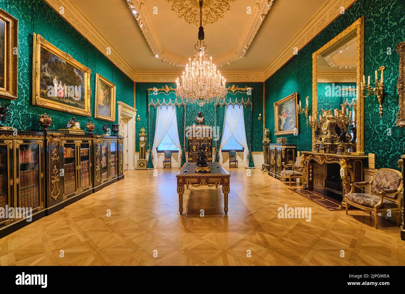 A green wallpaper room with a large, mirrored fireplace and a long cabinet of books. At the Wallace Collection Museum in London, England, United Kingd Stock Photo