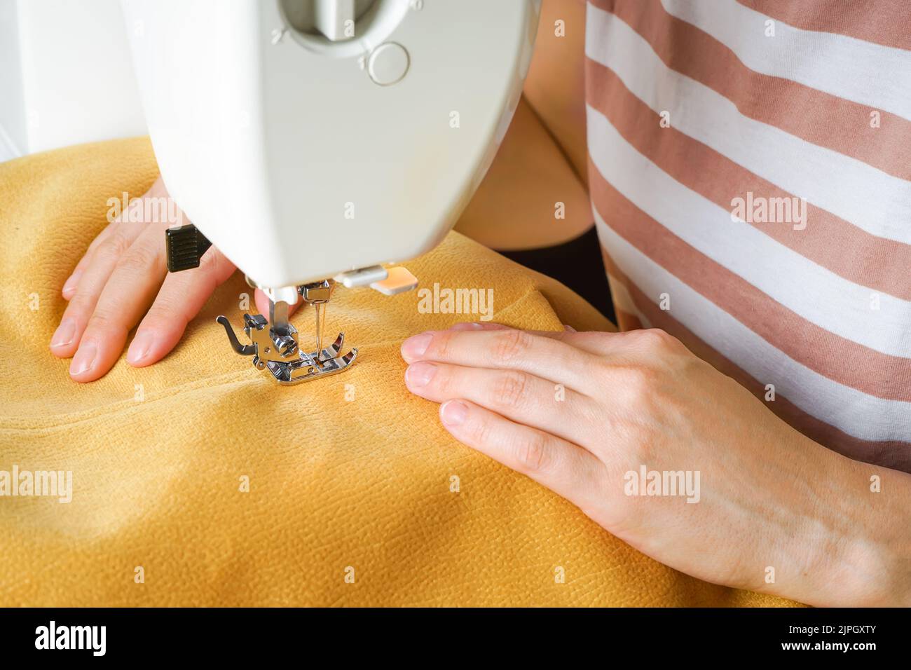 Seamstress female hands holding and stitching yellow textile fabric on