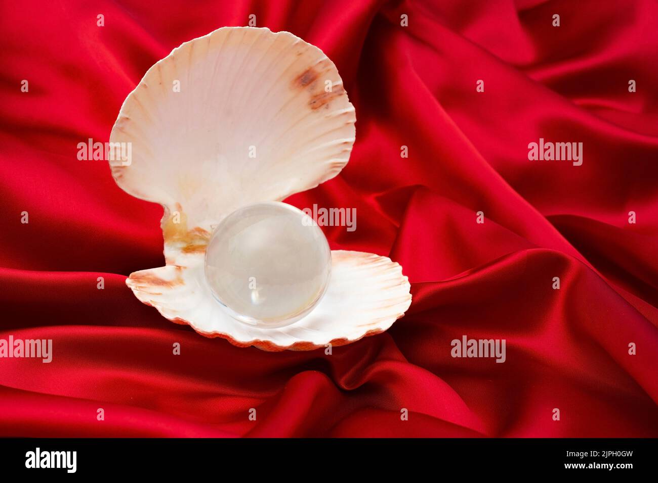 Opened sea shell with a big crystal lens ball, on red satin background, abstract valentines template. Stock Photo