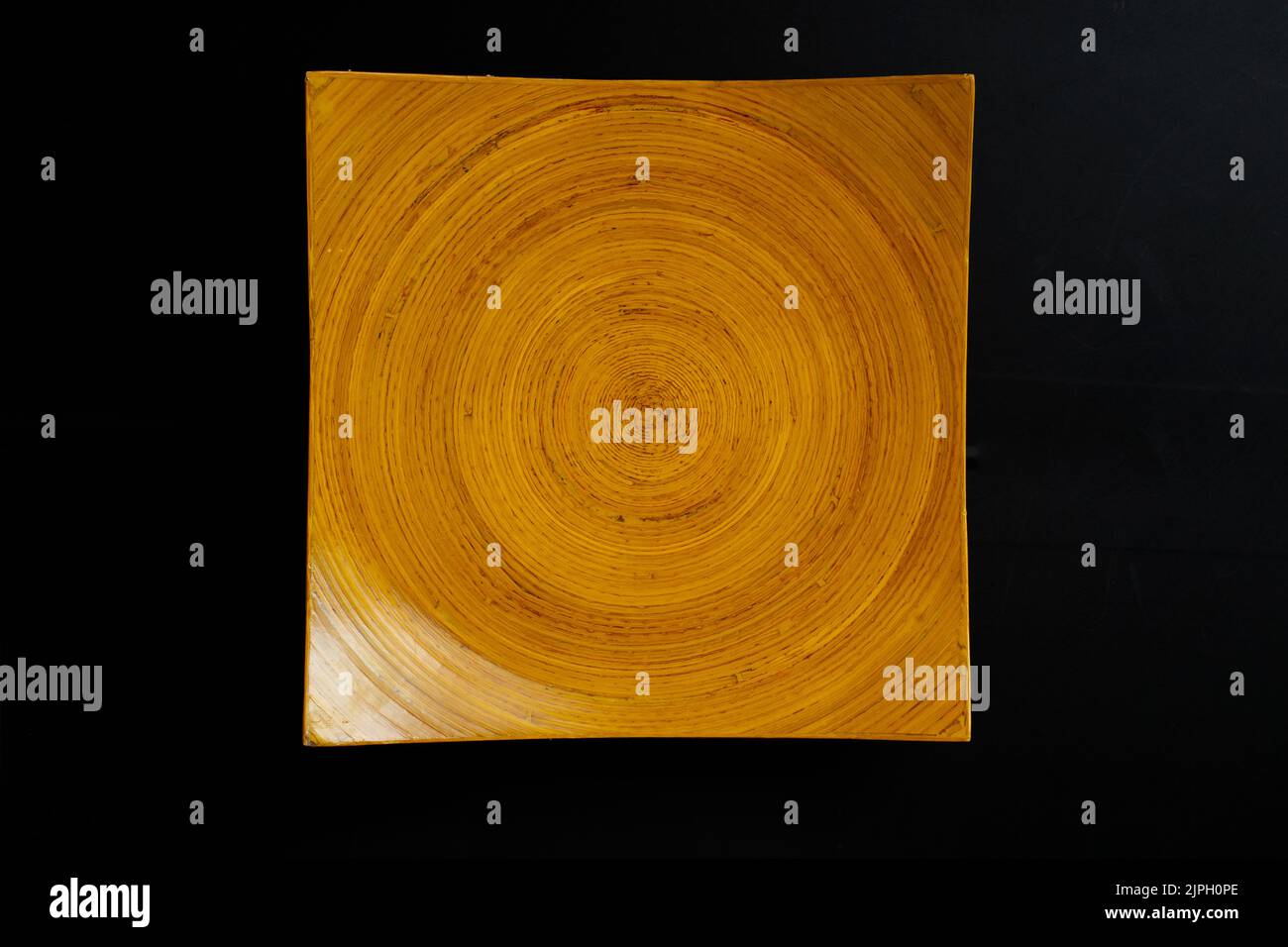 square wooden plate with concentric circles pattern. Orange textured dish isolated on black background. Stock Photo