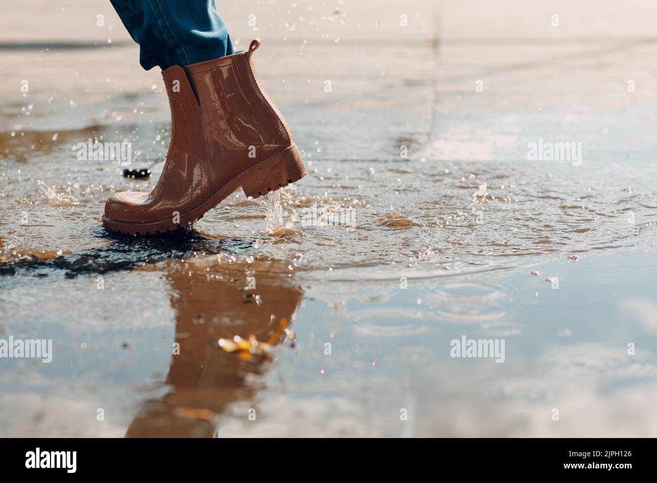 Woman wearing rain rubber boots walking running and jumping into puddle ...