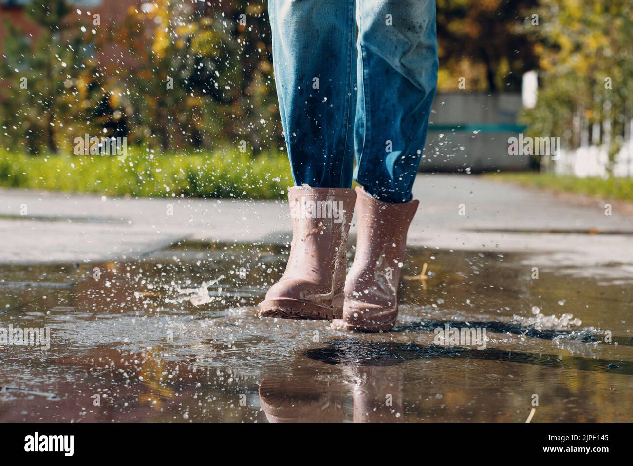 Woman wearing rain rubber boots walking running and jumping into puddle ...