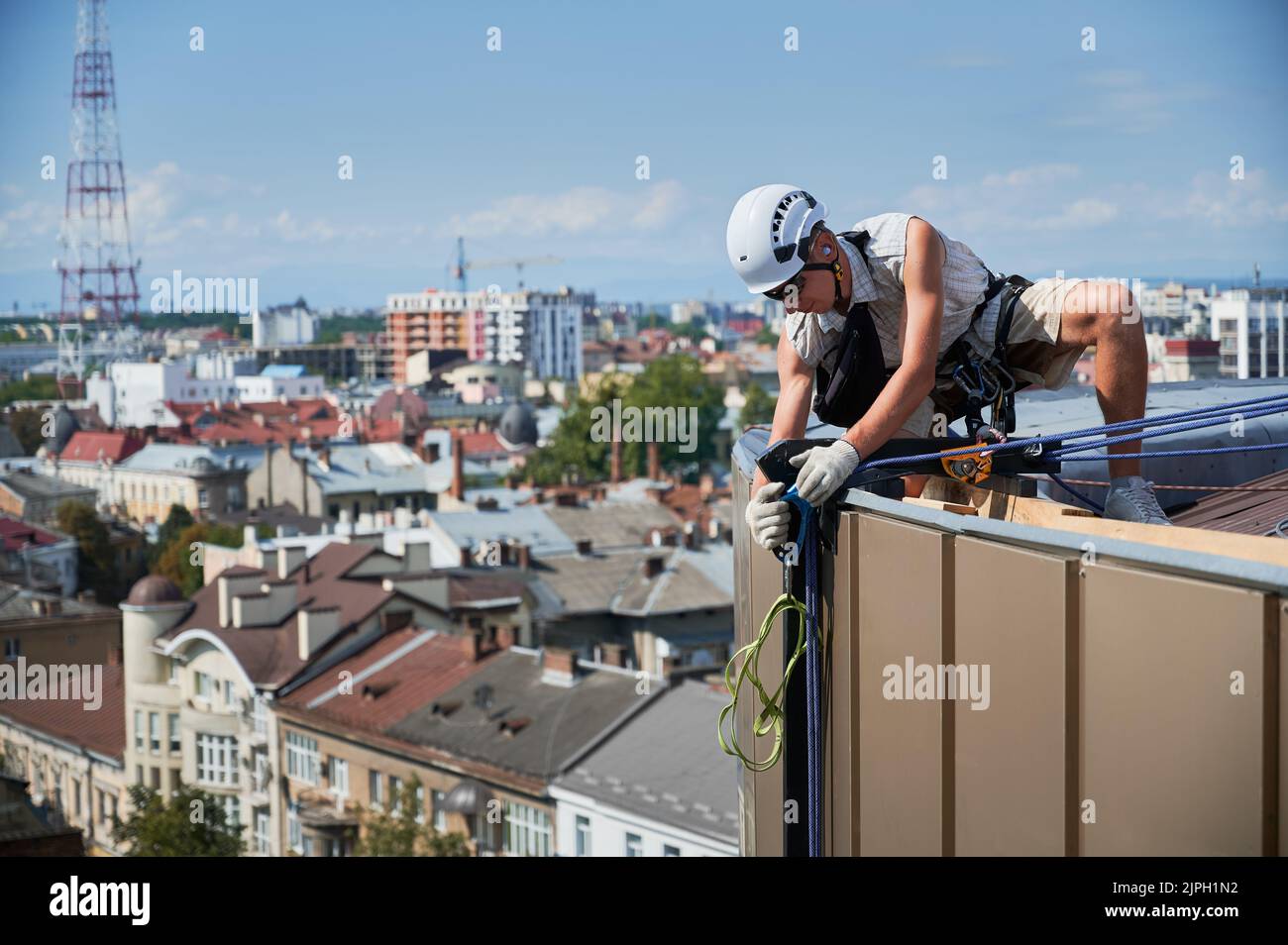 Industrial mountaineering worker in safety helmet crouching down on building roof and adjusting