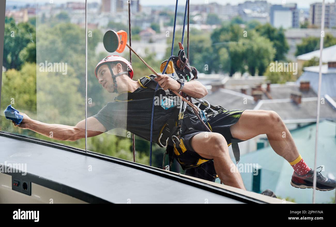 Industrial mountaineering cleaning service worker hanging on rope and