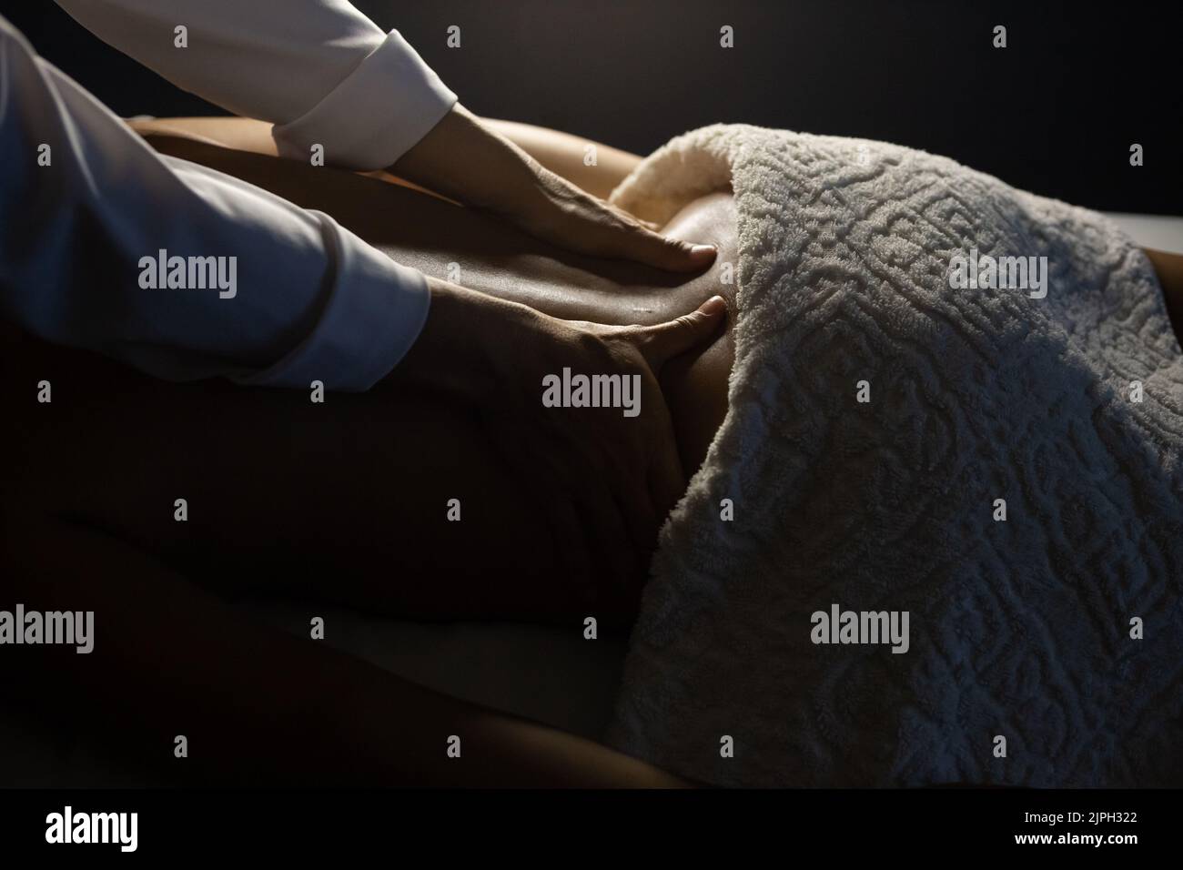 Goiânia, Goias, Brazil – July 18, 2022: Detail of a massage therapist massaging the back of a patient who is lying on a stretcher. Dark background. Stock Photo