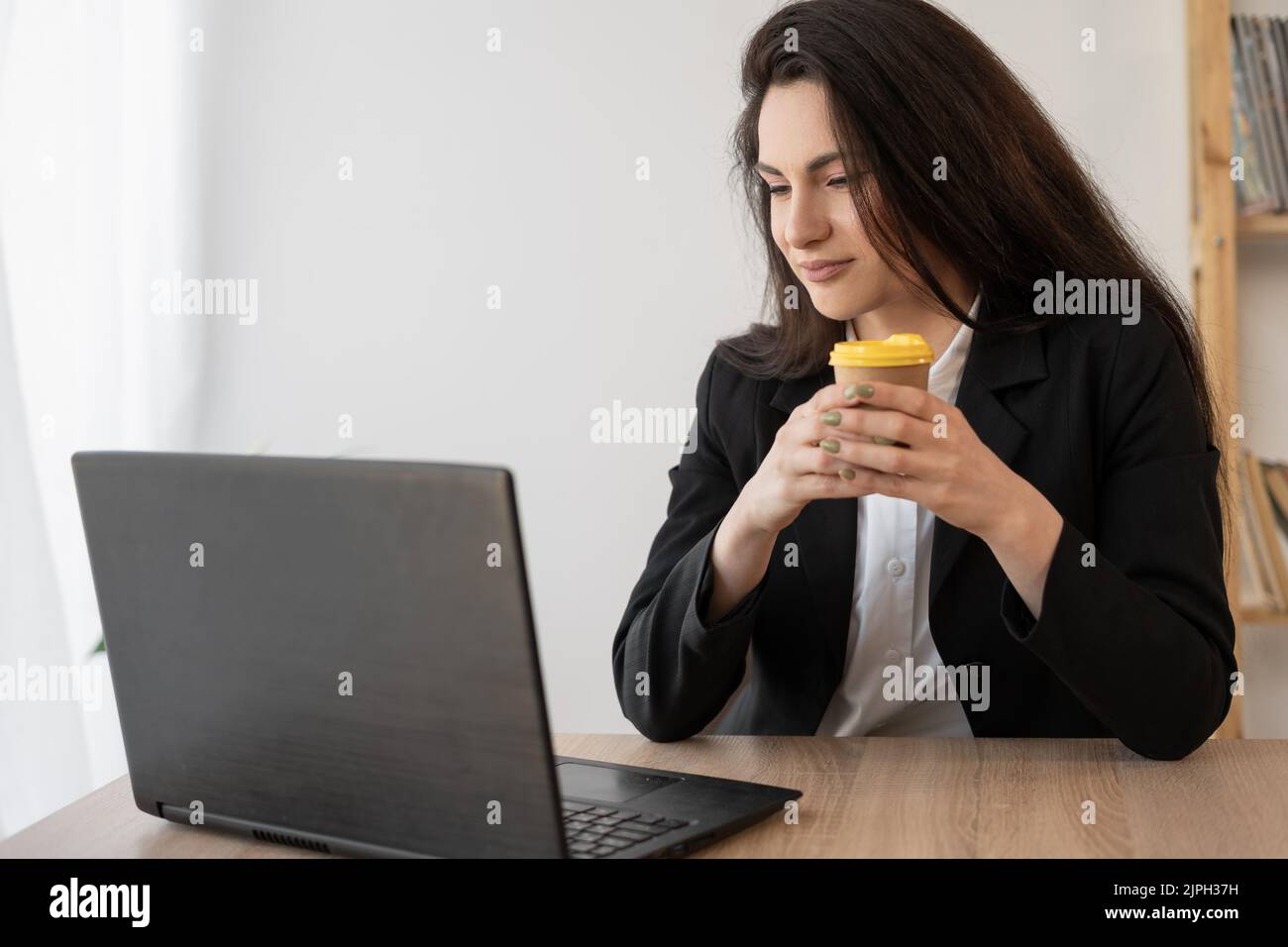 Adult happy hispanic businesswoman talking online chat meeting holding coffee using laptop in virtual office. College female student learning remotely Stock Photo