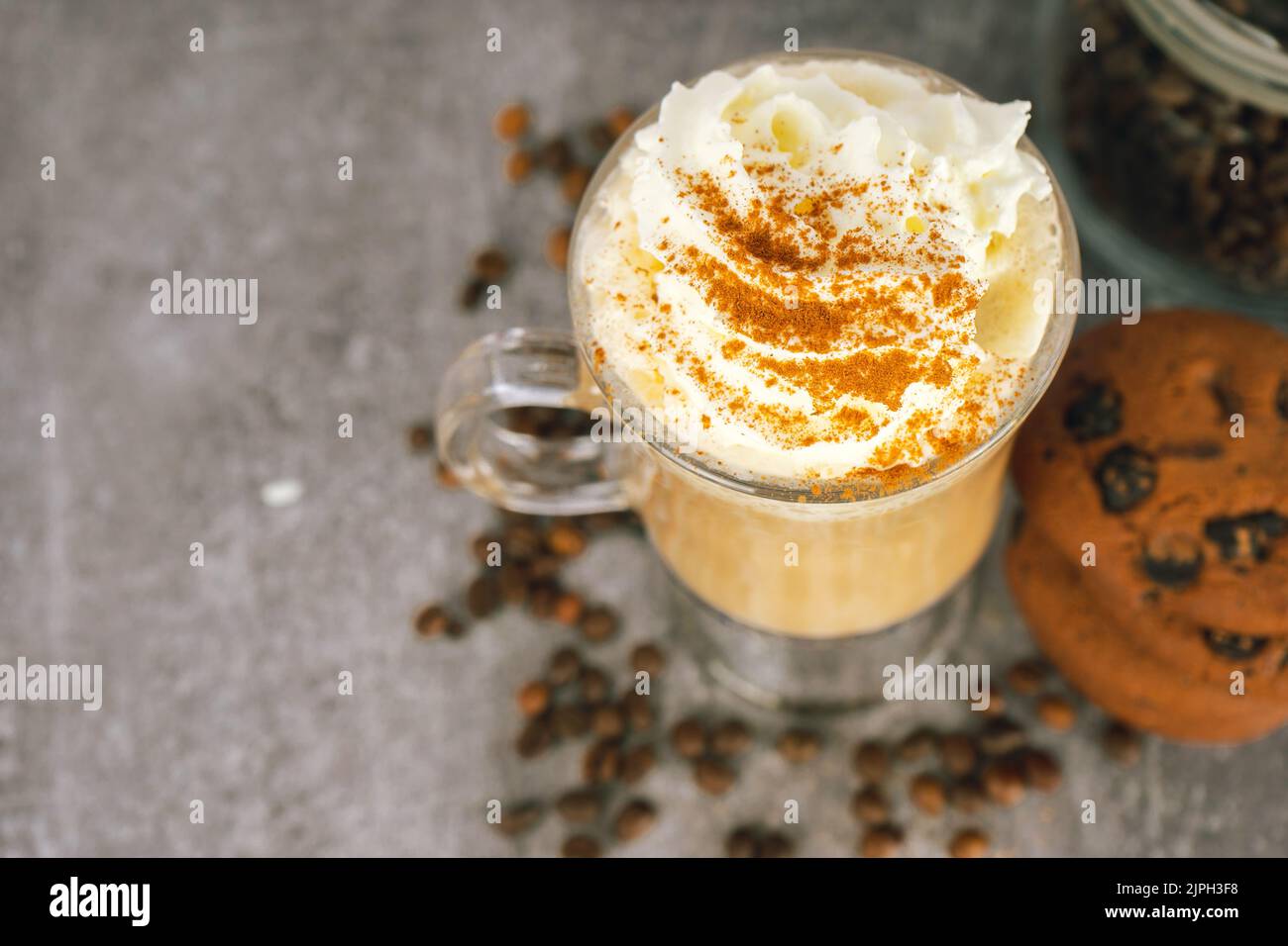 Iced caramel latte coffee in a tall glass with whipped cream on gray background with scattering