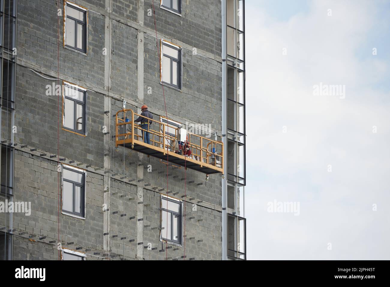 Builder works in a special suspended platform at the construction of an apartment building Stock Photo