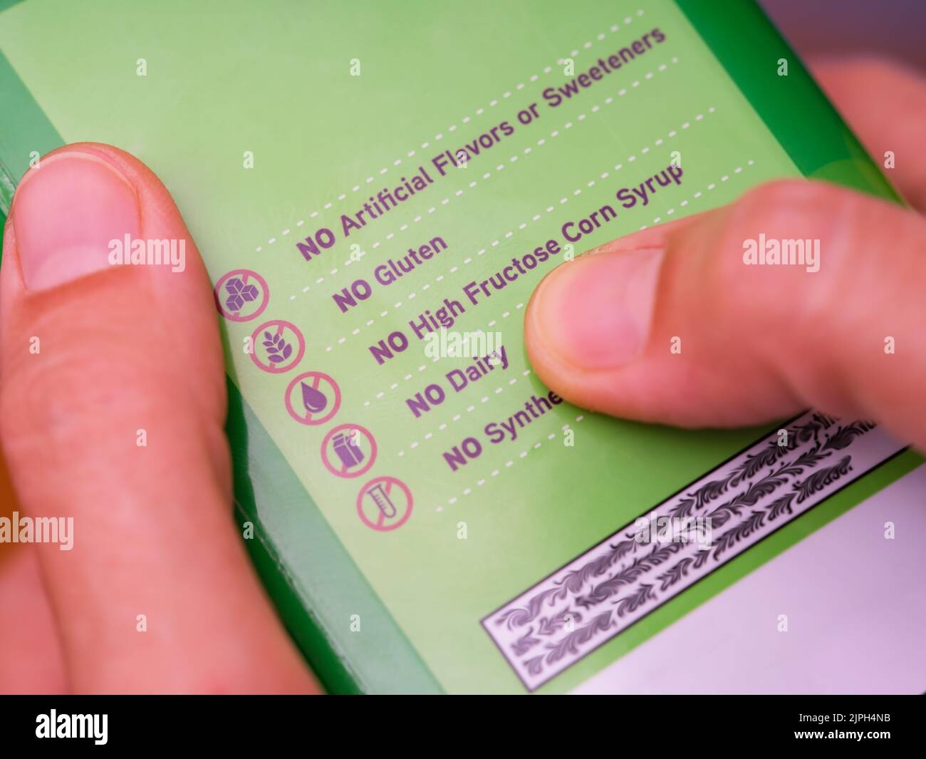 A woman reading a label with the words No Artificial Flavors or Sweeteners, No gluten, No high fructose corn syrup, No dairy, No synthetics. Stock Photo