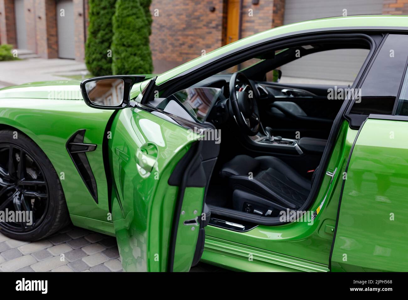 Modern green car with opened door is on parking near garage gate of ...