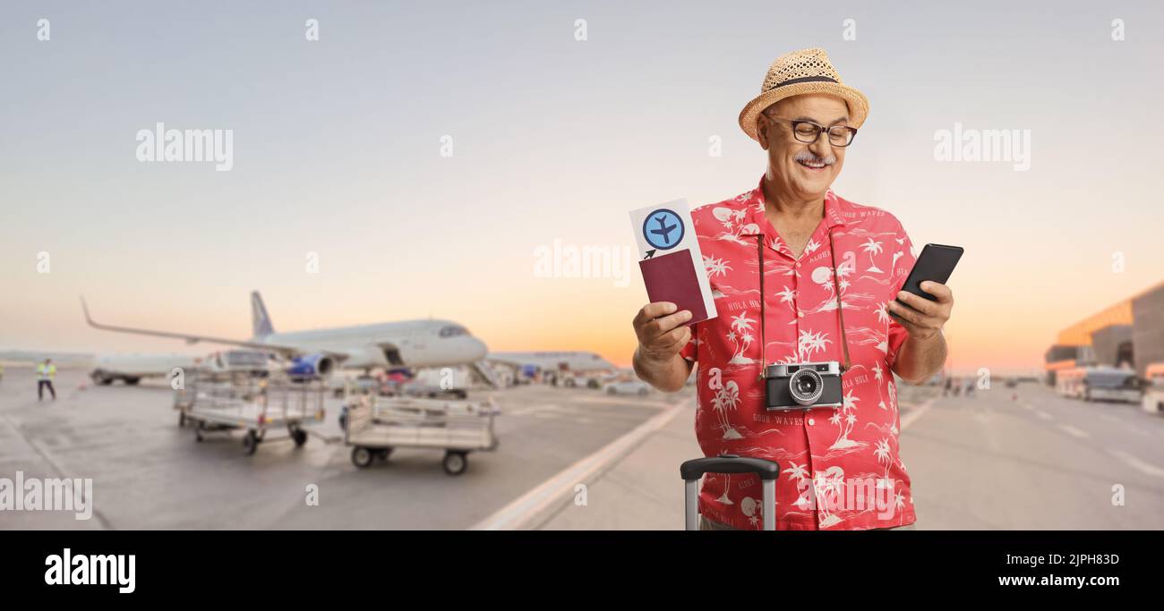 Mature male tourist holding a passport with a plane ticket and looking at a smartphone at an airport apron Stock Photo