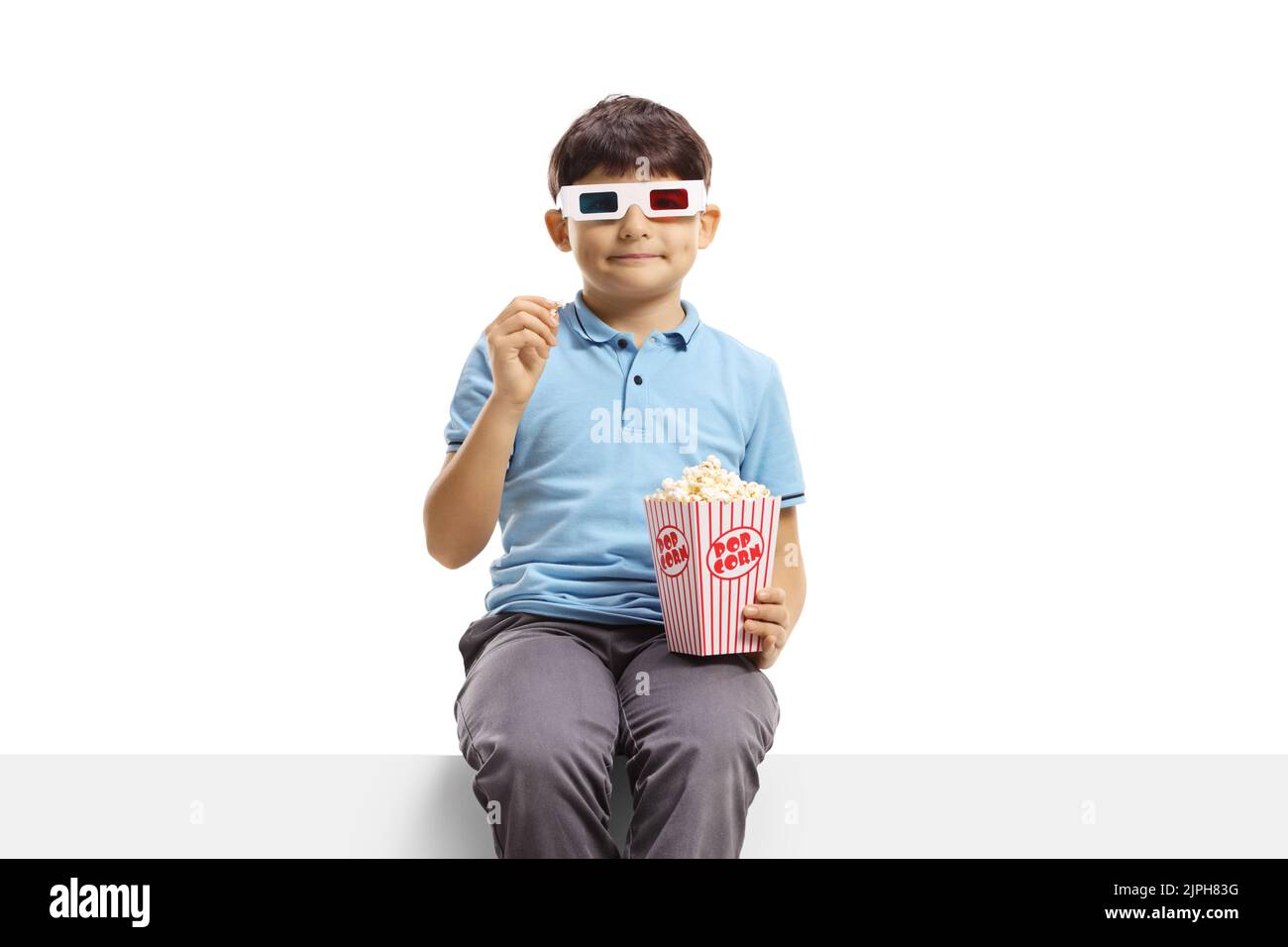 Boy with 3d cinema glasses sitting on a panel and eating popcorn isolated on white background Stock Photo