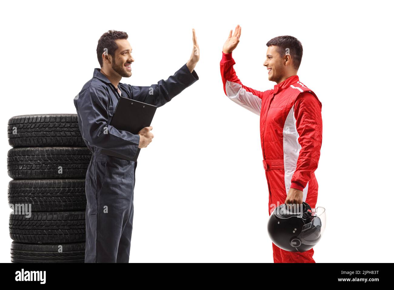 Auto mechanic standing next to a pile of tires and gesturing high five with a racer isolated on white background Stock Photo