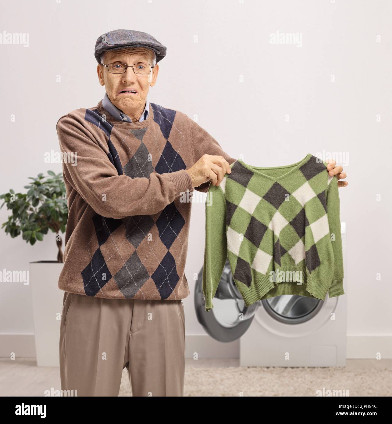Disappointed senior man holding a shrunken blouse inside a bathroom Stock Photo