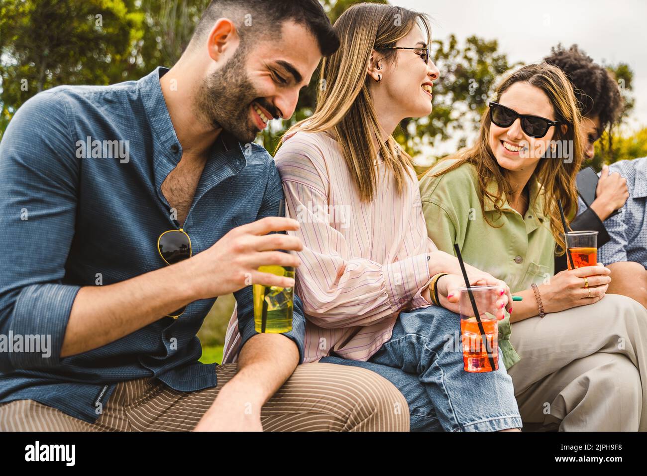 Group of happy friends sitting outdoors and having fun drinking cocktails on plastic glasses - alcohol and people lifestyle concept Stock Photo