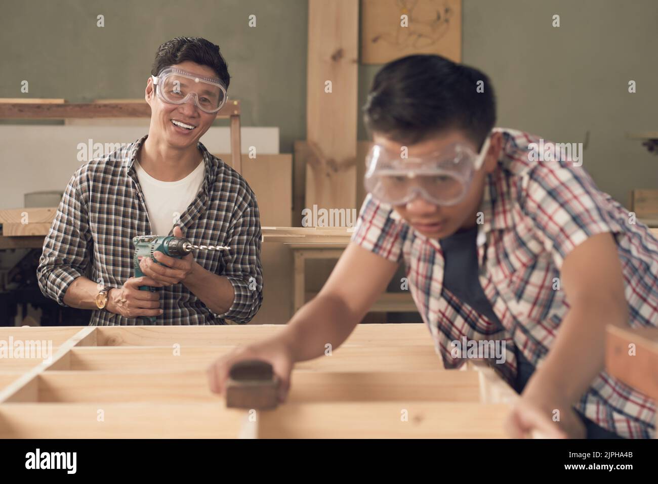 Happy Vietnamese carpenter with drill working with his son Stock Photo