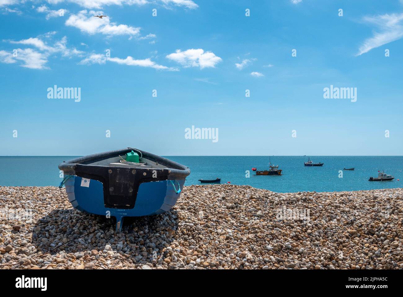 blue boat on a deserted beach at Selsey West Sussex England with blue sky sea and fishing boats in the background Stock Photo