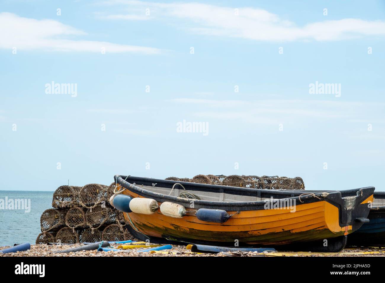 lobster pots traps and orange boat on the beach at Selsey West Sussex England with the sea and blue sky in the background Stock Photo