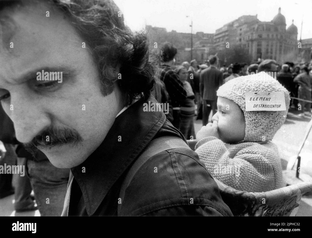 Bucharest, Romania, April 1990. 'Golaniada', a major anti-communism protest  in the University Square following the Romanian Revolution of 1989. People would gather daily to protest the ex-communists that grabbed the power after the Revolution. A father is carrying his baby, tagged as a 'destabilizing element'. This came after the state-controlled media called the protesters various injurious names. Stock Photo