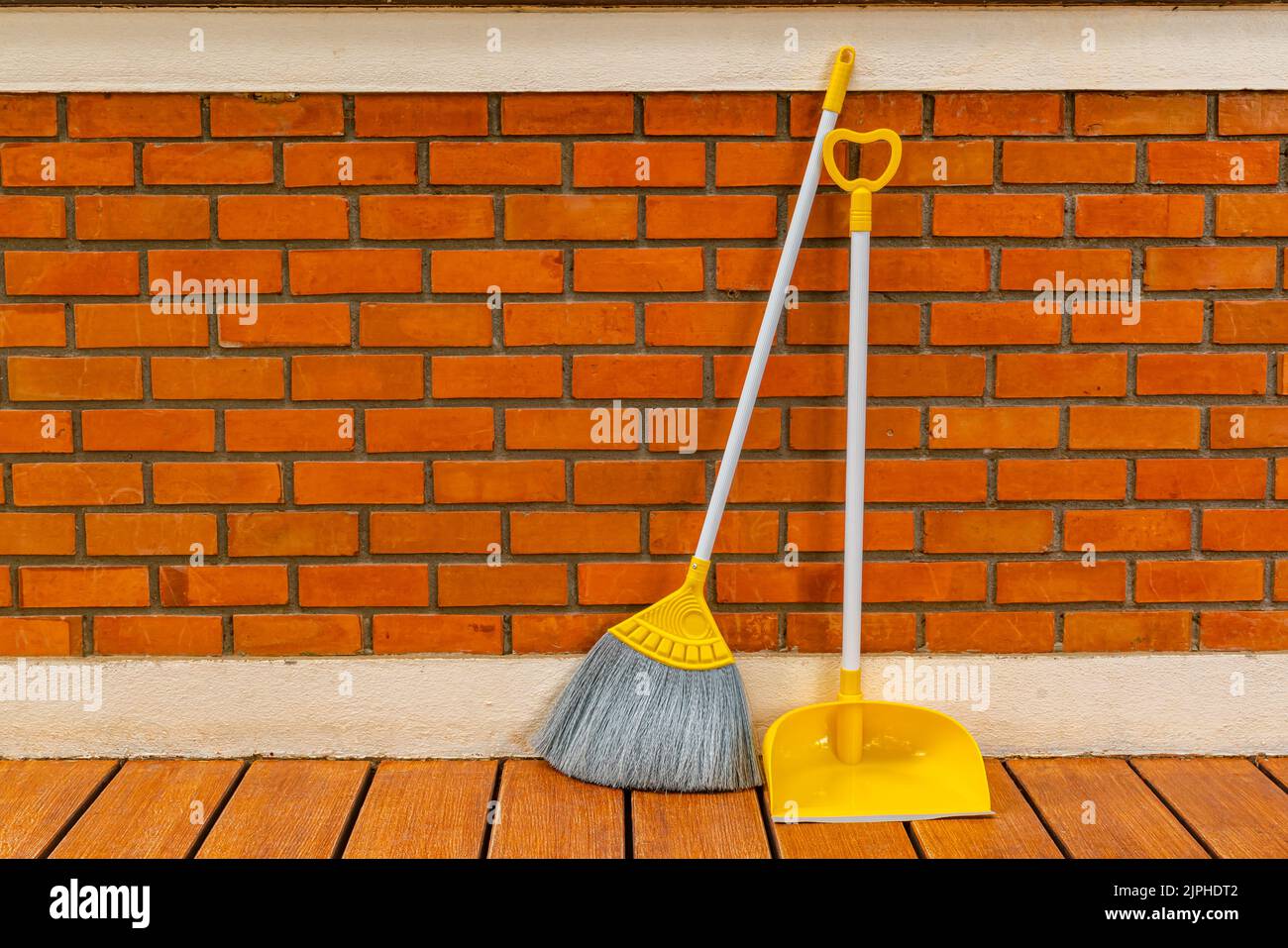 Long handle plastic yellow broom and dustpan prop against a red brick wall of a house. Stock Photo