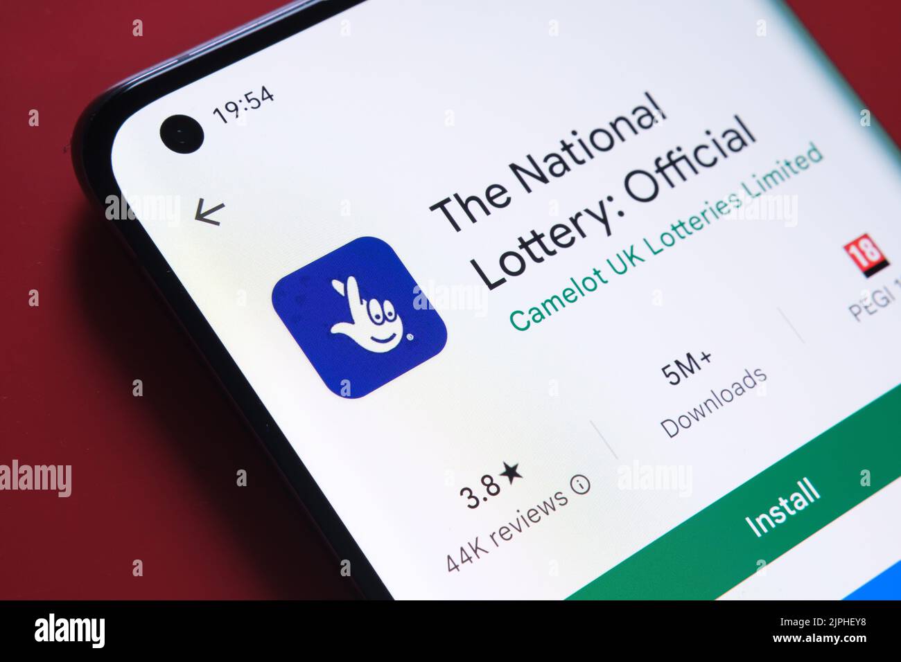 The national Lottery app seen in Google Play Store on the smartphone screen placed on red background. Close up photo with selective focus. Stafford, U Stock Photo