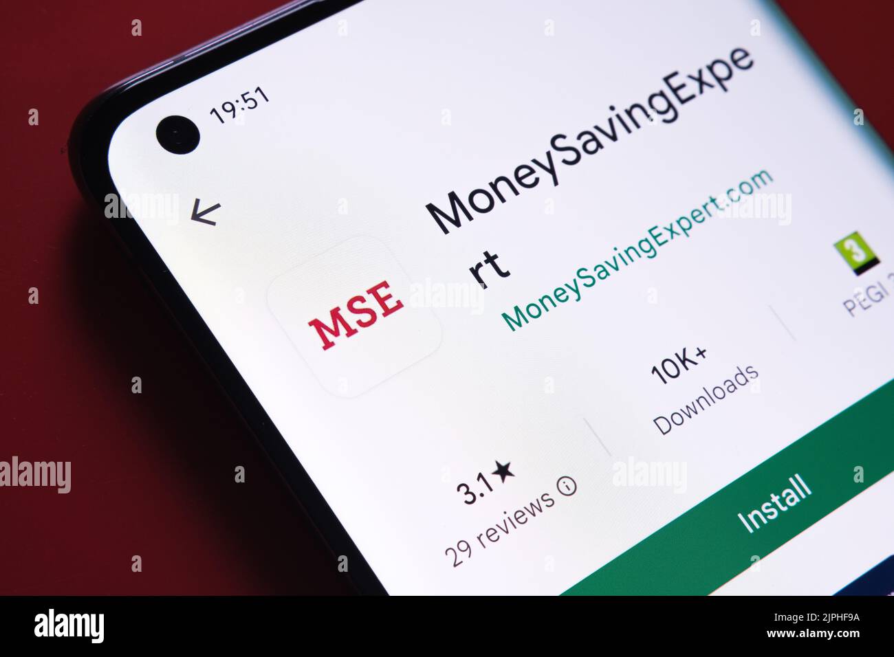 moneysavingexpert app seen in Google Play Store on the smartphone screen placed on red background. Close up photo with selective focus. Stafford, Unit Stock Photo