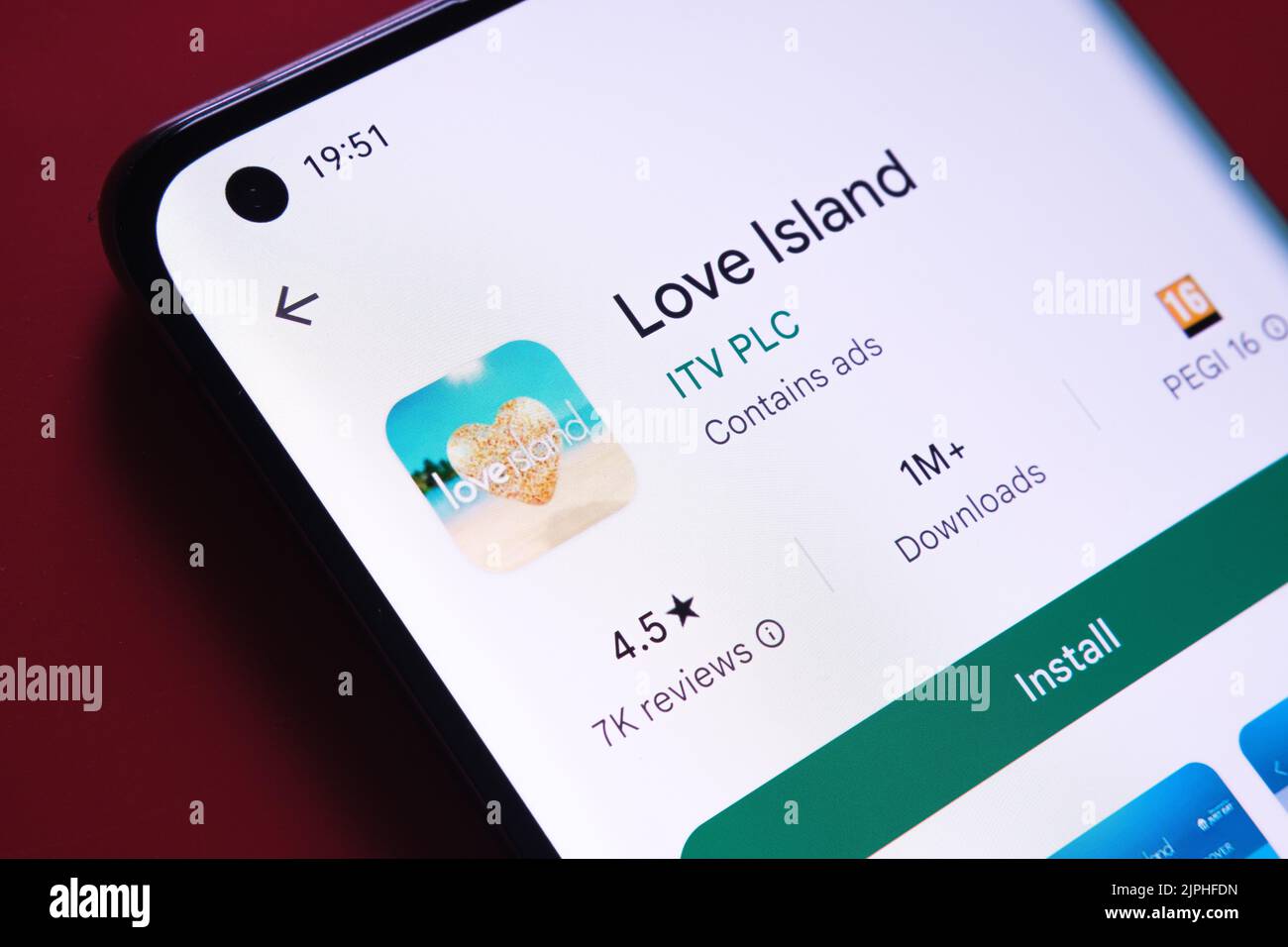 Love Island app seen in Google Play Store on the smartphone screen placed on red background. Close up photo with selective focus. Stafford, United Kin Stock Photo