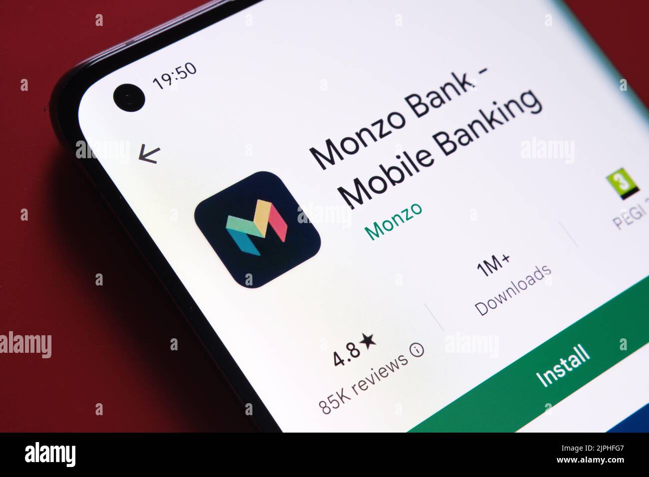 monzo app seen in Google Play Store on the smartphone screen placed on red background. Close up photo with selective focus. Stafford, United Kingdom, Stock Photo