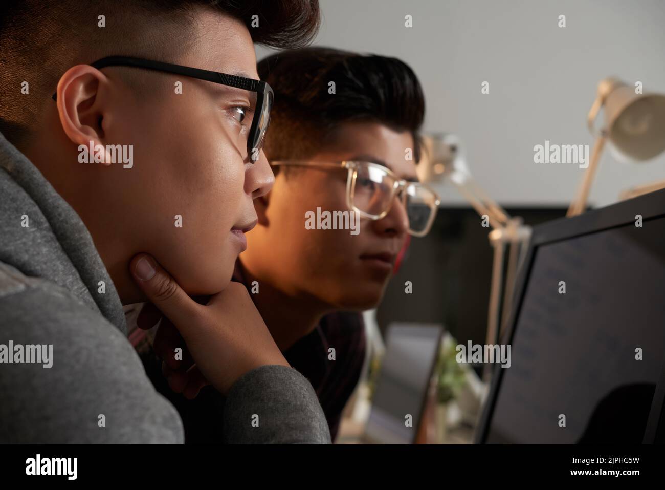 Close-up shot of curious Asian students wearing eyeglasses brainstorming on joint university project while gathered together at home Stock Photo