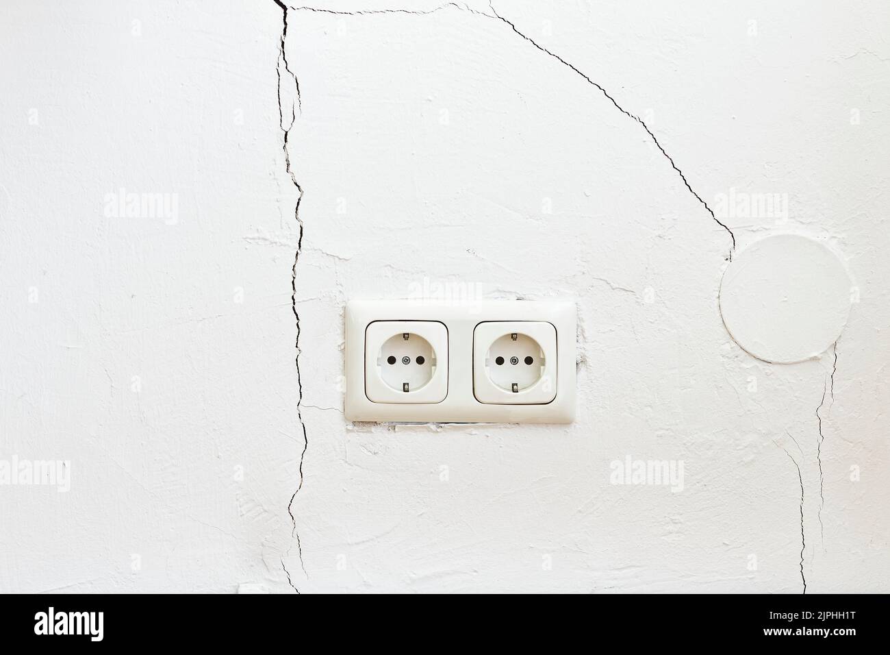 Damaged property: white wall with cracks or rips and two european plug sockets or outlets. Refurbishment of real estate concept. Stock Photo