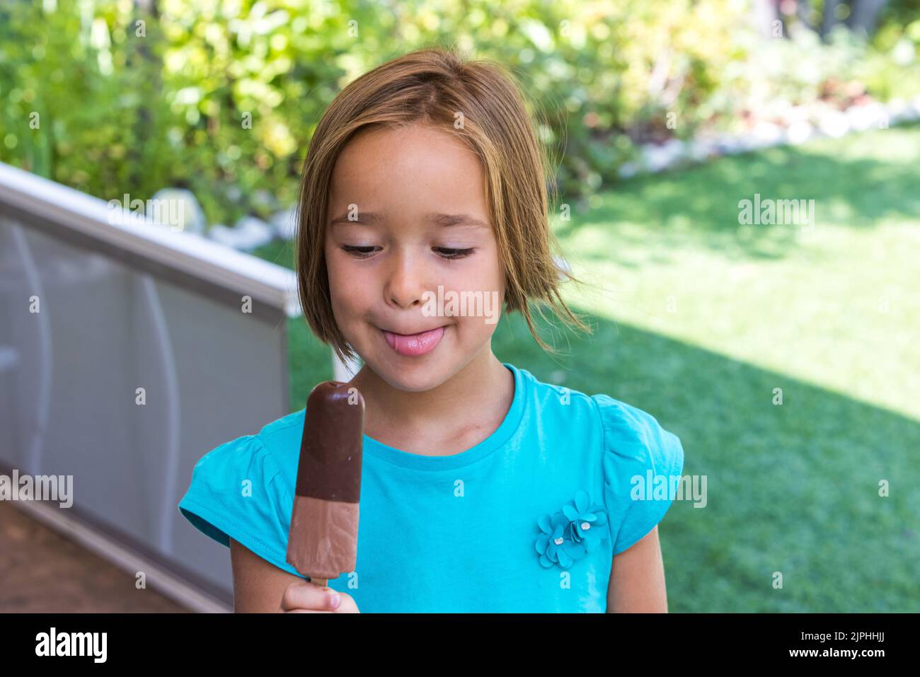 Girl wearing green tshirt, holding a milk chocolate ice cream, in the street, in summer